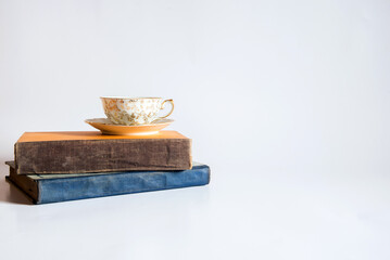 Libros y una taza de té pequeña con adornos de flores doradas pintadas a mano sobre un fondo blanco. Concepto de lectura mientras bebe una bebida herbal tibia y saludable