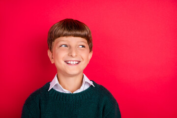 Photo of dreamy charming school boy wear knitted pullover smiling looking empty space isolated red color background