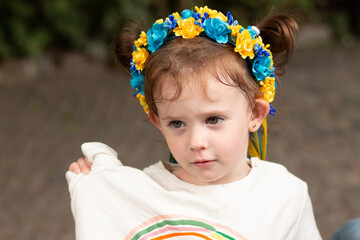 Little redhead preschooler girl with pigtails in national ukrainian folk decoration wreath outdoors