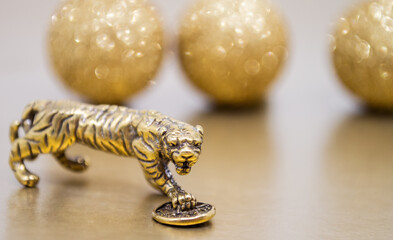 A bronze figure of a tiger with a coin - the symbol of the Chinese new year 2022 on a background of golden glitter balls, a copy space. Wishes of good luck, financial well-being and wealth
