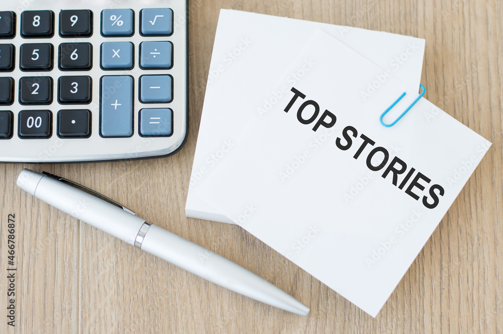 Poster white card with top stories text on the table next to calculator and pen