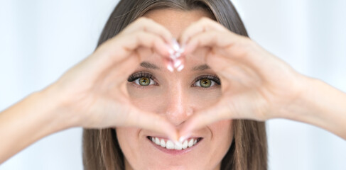 Eye care. Healthy eyes. Young woman with perfect vision makes heart shape with hands. Ophthalmology concept