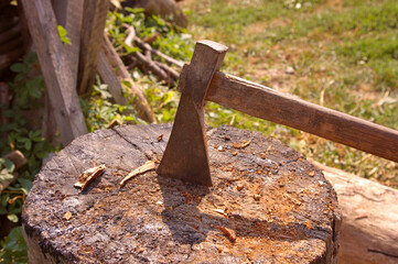 Metal ax blade with wooden handle used to shape, split and cut wood or as a heraldic symbol. Old socketed wooden ax stuck in a wooden log. 