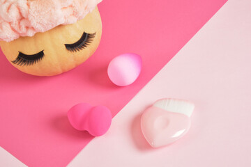 pumpkin in a headband and false eyelashes on a pink background, sponges for applying makeup beauty...