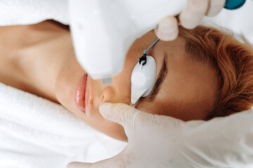 Naklejka premium Close up cosmetologist arm making depilation of face for female client. Ginger woman laying at the clinic during her treatment
