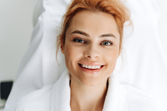 Top view of ginger woman laying at the couch after making an effective facial procedure. Woman laying with pleasure smile. Stock photo