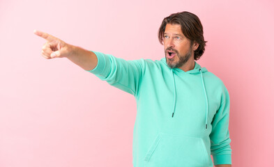 Senior dutch man isolated on pink background pointing away