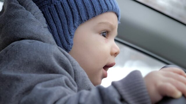 A Little Boy Is Kneeling By His Dad At The Wheel Of A Car. The Boy Turns The Steering Wheel Of The Car And Licks It. The Child And Dad Spend Time Together. Close-up