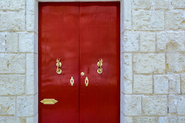 Red wooden door with golden vintage knockers as dolphin with a trident-shaped tails and golden...