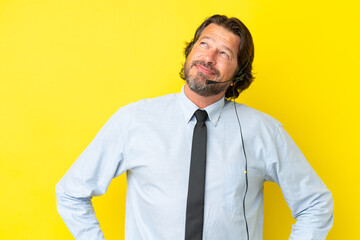 Telemarketer dutch man working with a headset isolated on yellow background posing with arms at hip and smiling