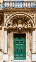 Obraz premium Historical ornate wooden green door in a stone entry in Mdina, Malta. With stone arched carvings above. Architectural theme.