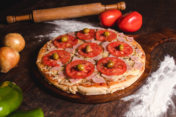 Mozzarella pizza with tomato and olives and different vegetables around on a wooden table.