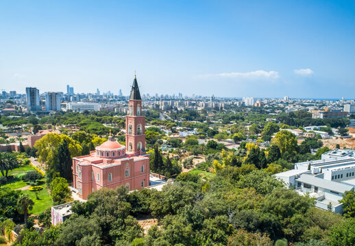 Aerial view of the red Saint Peter and Saint Tabitha Orthodox Church with the surrounding gardens and Tel-Aviv city skyline, Tel-Aviv, Israel.