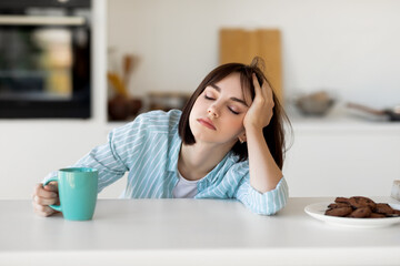 Sleepy young woman drinking coffee, feeling tired, suffering from insomnia and sleeping disorder,...