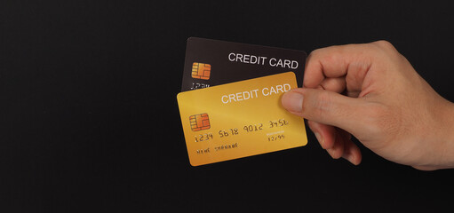 Two credit cards in black and gold color in hand on black background.