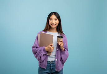 Fototapeta premium Excited asian female student holding notebooks and coffee to go, having break while studying, blue background