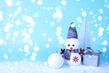 Snowman, gift, tree, Christmas ball on white snow on a blue background in snowflakes. Christmas New Year card.