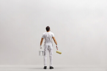 Rear view shot of a painter in front of a wall holding a bucket ana a paint roller