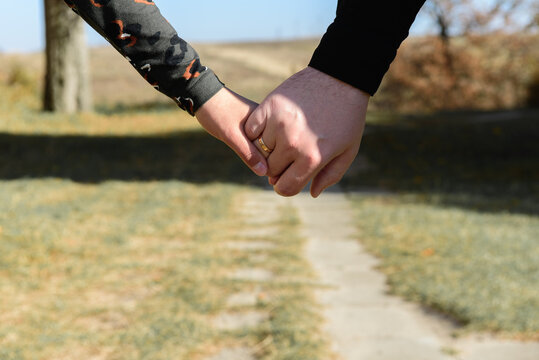 young couple holding hands in autumn or summer park at sunset. Close up of a loving couple holding hands while walking. Selective focus