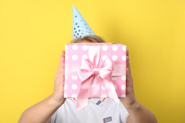 Woman in party hat holding gift box on yellow background