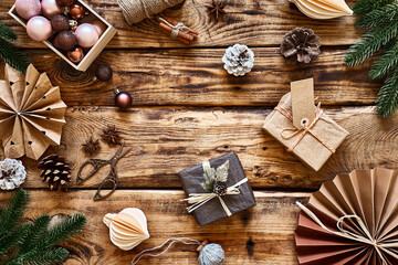 Winter holiday decoration. Christmas gifts wrapped in craft recycled paper, paper snowflakes, fans on wooden table. Nature aesthetic. Zero waste handmade gits. DIY.