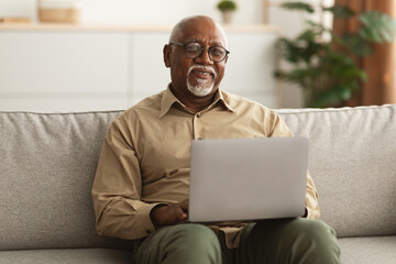 Mature Black Man Using Laptop Smiling To Camera At Home