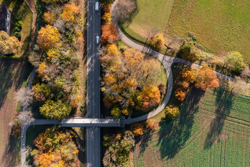 Top down view at a autumnal landscape with a rural street and a covered bridge for pedestians straight from above in Oberhaching.