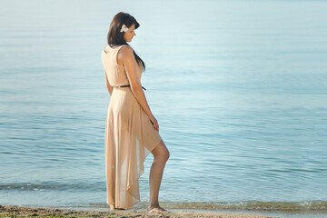 girl with black hair in a beige dress on the shore of the ocean