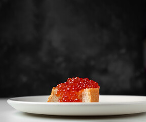 A slice of bread with salmon red caviar on a white plate