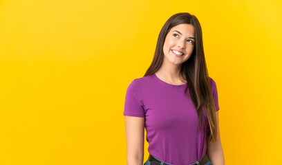 Teenager Brazilian girl over isolated yellow background thinking an idea while looking up