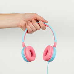 Pink-blue headphones in hand on a white background. Music services, podcasts, and streaming audio.