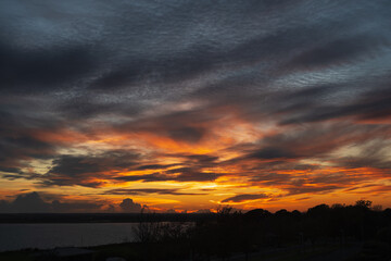 Low clouds forming a dramatic, fiery sky at sunset over water.