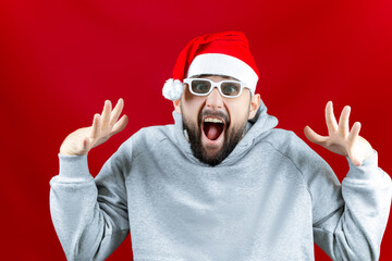Naklejka premium on a red Christmas background, a man in a Santa Claus hat and with glasses for watching movies, a man screams from what he saw