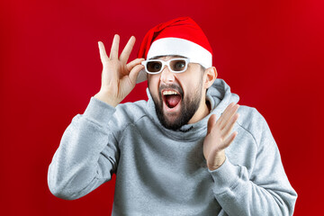 on a red Christmas background, a man in a Santa Claus hat and with glasses for watching movies, a man screams from what he saw