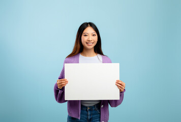 Advertisement concept. Happy asian lady holding empty blank placard, standing over blue studio background