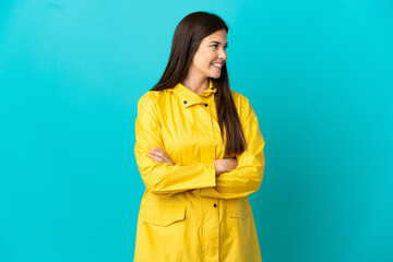 Teenager Brazilian girl wearing a rainproof coat over isolated blue background looking side