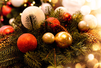 Christmas arrangement with pine twigs, red, white, gold balls, cones on the background of a christmas tree with beautiful bokeh.