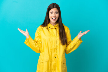 Teenager Brazilian girl wearing a rainproof coat over isolated blue background with shocked facial expression