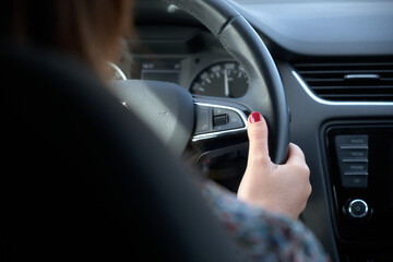Detail of a woman's hand holding a steering wheel and driving a car
