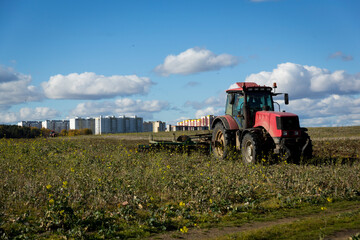 A farmer in a tractor, agricultural machinery, prepares the land with a cultivator. A modern red tractor in a field. Plowing a heavy tractor while cultivating agricultural work in a field with a plow.