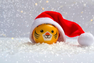 The symbol of the new year is a tiger in a Santa hat on the snow against a background of bokeh lights. Close up of new year