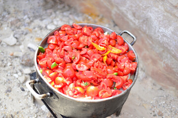 man cooking tomato soup on camp fire. wild nature resting. cutting tomatoes. Chopped juicy canned tomatoes in big bowl, tomato soup