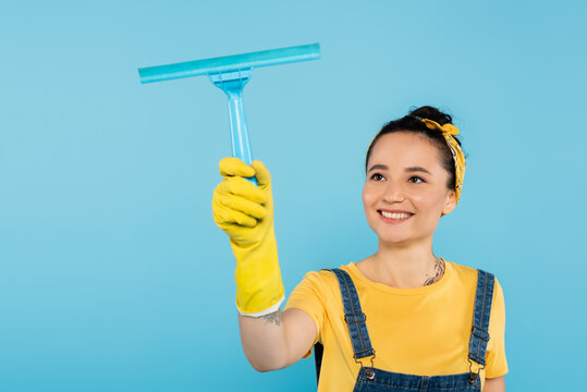 Pleased Woman In Yellow Rubber Glove Holding Window Cleaner Isolated On Blue.