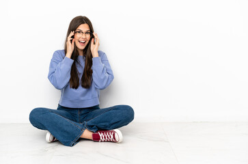 Young woman sitting on the floor with glasses and surprised