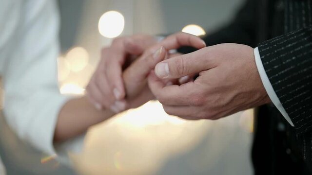 hands of newlyweds in wedding day, groom is holding and stroking palm of bride
