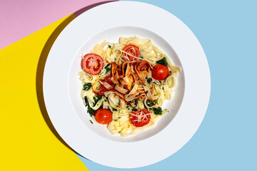 Italian pasta with bolognese sauce, cherry tomatoes, spinach in a white plate on a multi-colored trendy background.