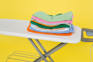 stack of clean laundry on ironing board isolated on yellow.