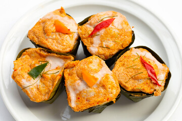 Thai streamed fish curry in banana leaves on white.