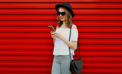 Portrait of happy smiling young woman with smartphone on red background