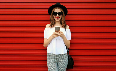 Portrait of happy smiling young woman with smartphone on red background